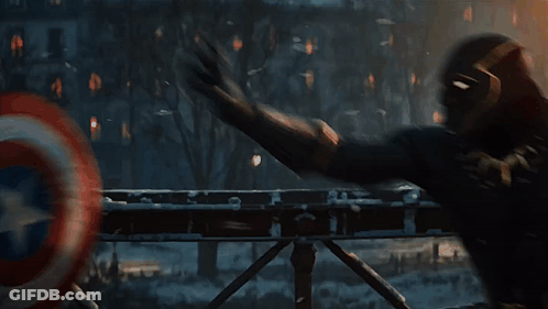 A Man In A Black Suit Is Holding A Red And White Shield . GIF