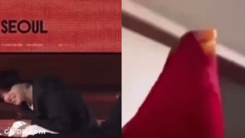 A Man In A Black Suit Is Laying On A Bed Next To A Red Item . GIF