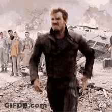 A Man In A Black Suit Is Running In Front Of A Group Of People In A Field . GIF