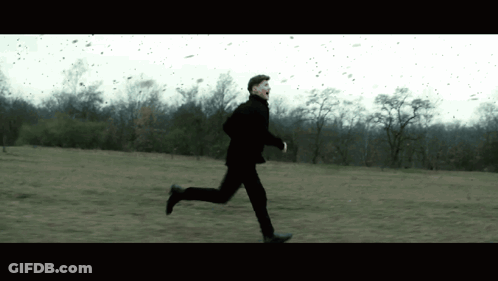 A Man In A Black Suit Is Running Through A Field GIF