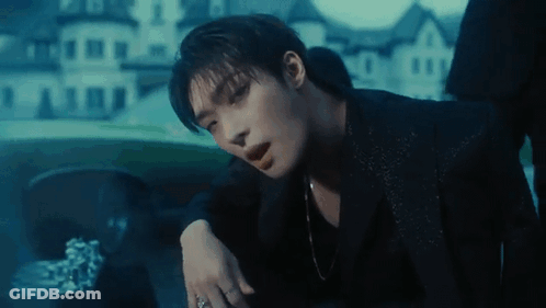 A Man In A Black Suit Is Sitting In A Car With His Hand On His Shoulder . GIF