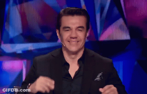 A Man In A Black Suit Is Smiling In Front Of A Blue Background GIF