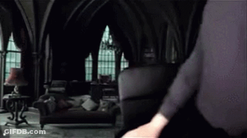 A Man In A Black Suit Is Standing In A Dark Room . GIF