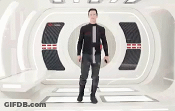 A Man In A Black Suit Is Standing In A Futuristic Room Holding A Gun . GIF