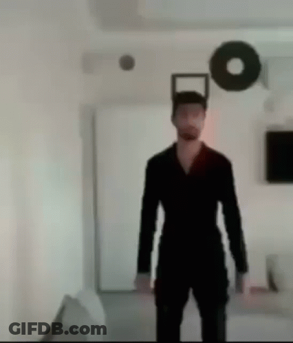 A Man In A Black Suit Is Standing In A Room With A Circle On The Wall . GIF