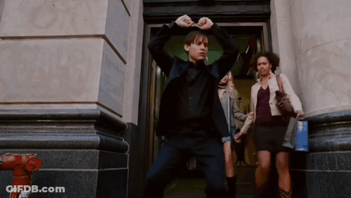 A Man In A Black Suit Is Standing In Front Of A Building GIF