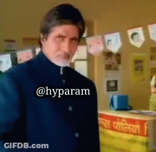 A Man In A Black Suit Is Standing In Front Of A Counter With A Sign That Says ' @Hyparam ' On It GIF
