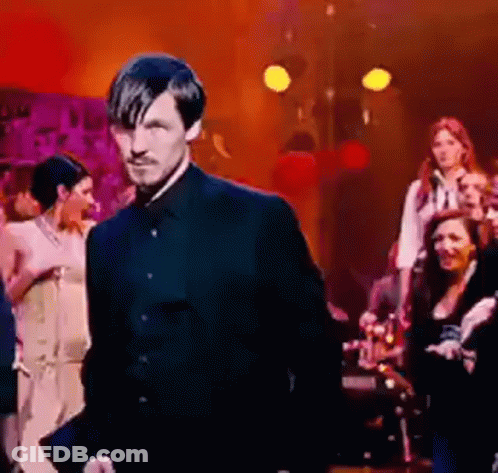 A Man In A Black Suit Is Standing In Front Of A Group Of People . GIF