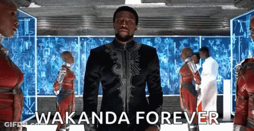 A Man In A Black Suit Is Standing In Front Of A Group Of People With The Words Wakanda Forever . GIF