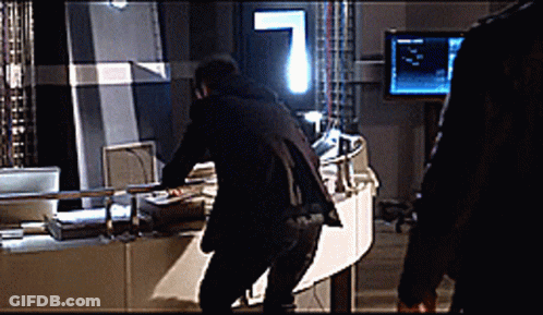 A Man In A Black Suit Is Standing In Front Of A Monitor GIF