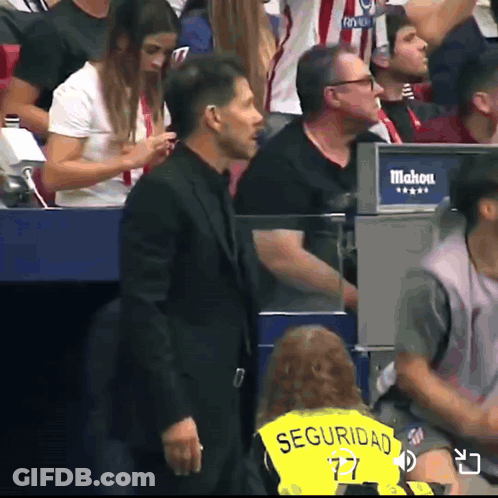 A Man In A Black Suit Is Standing In Front Of A Sign That Says Mahou GIF