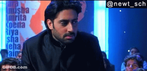 A Man In A Black Suit Is Standing In Front Of A Sign That Says Riya GIF