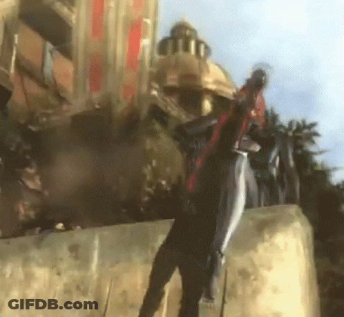 A Man In A Black Suit Is Standing On A Wall With A Building In The Background GIF