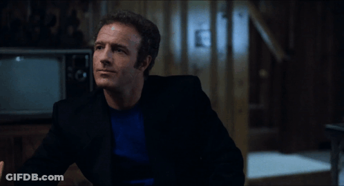 A Man In A Black Suit Is Talking To Another Man In A Blue Shirt GIF