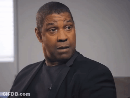 A Man In A Black Suit Looks At The Camera With A Serious Look On His Face GIF