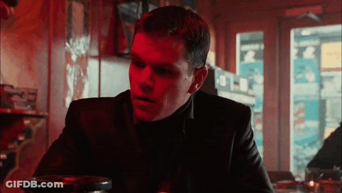 A Man In A Black Suit Sits At A Table In A Restaurant GIF