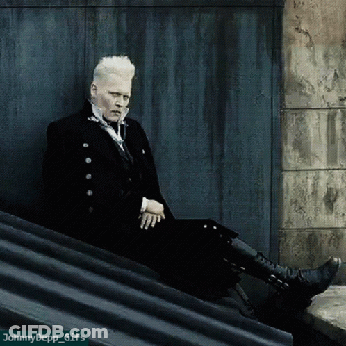 A Man In A Black Suit Sits On A Ledge With A Watermark That Says Johnny Depp GIF
