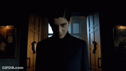 A Man In A Black Suit Stands In A Dark Hallway GIF