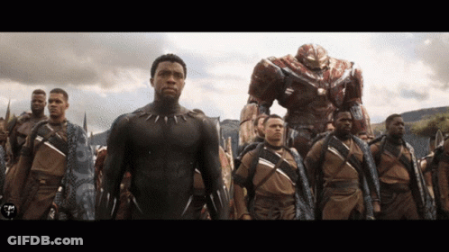 A Man In A Black Suit Stands In A Line With Other Men GIF