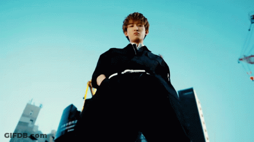 A Man In A Black Suit Stands In Front Of A Building That Says ' Tokyo ' On It GIF