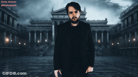 A Man In A Black Suit Stands In Front Of A Building With The Name Emilia At The Top GIF