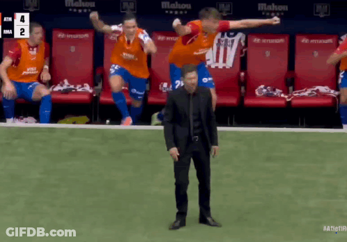 A Man In A Black Suit Stands In Front Of A Group Of Soccer Players On The Field GIF