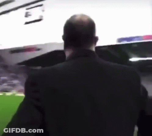 A Man In A Black Suit Stands In Front Of A Stadium GIF