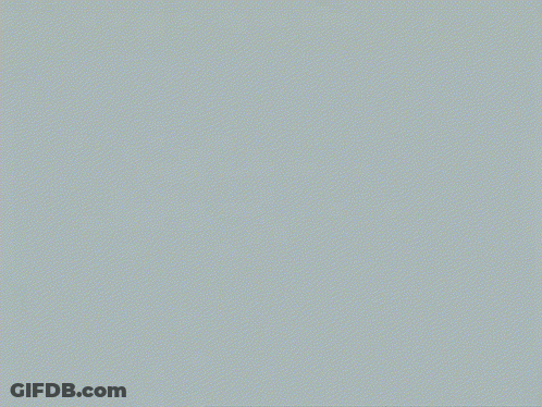 A Man In A Black Suit Stands In Front Of A White Background GIF