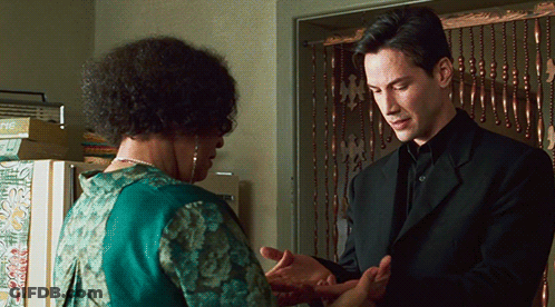 A Man In A Black Suit Stands Next To A Woman In A Green Dress GIF