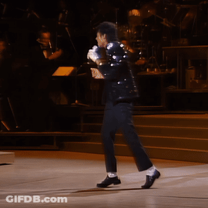 A Man In A Black Suit Stands On A Stage Holding A Microphone GIF