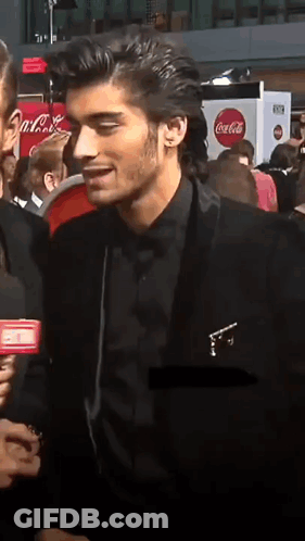 A Man In A Black Suit Talks Into A Microphone In Front Of A Coca-Cola Sign GIF