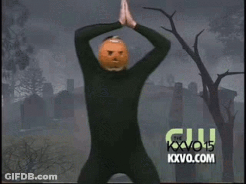 A Man In A Black Suit With A Pumpkin On His Head Is Dancing In A Cemetery . GIF