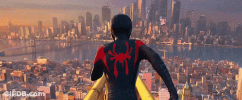 A Man In A Black Suit With A Red Spider On His Back Stands In Front Of A City Skyline GIF