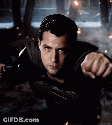 A Man In A Black Superman Costume Is Flying In The Air GIF