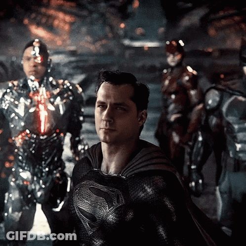 A Man In A Black Superman Costume Is Standing In Front Of A Group Of Robots GIF