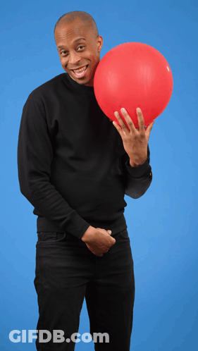 A Man In A Black Sweater Is Holding A Red Balloon In Front Of His Face GIF