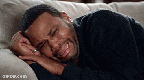 A Man In A Black Sweater Is Laying On A Couch Crying . GIF