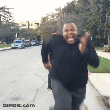 A Man In A Black Sweater Is Running Down A Street And Making A Funny Face GIF