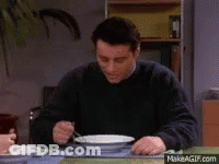 A Man In A Black Sweater Is Sitting At A Table Eating From A Bowl With A Fork . GIF