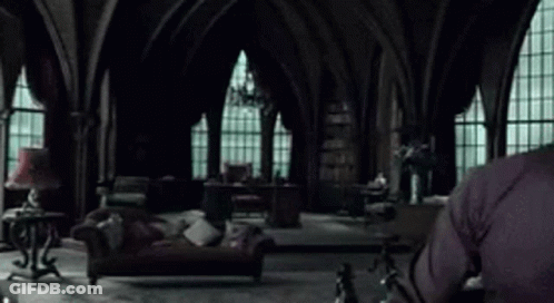 A Man In A Black Sweater Is Sitting In A Living Room With A Couch And A Lamp . GIF