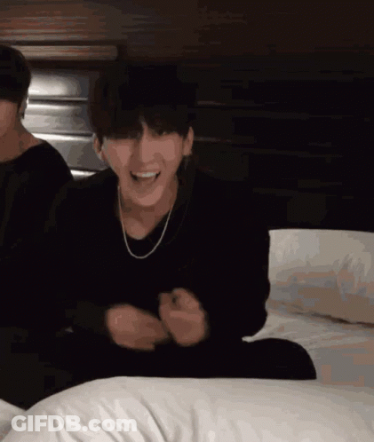 A Man In A Black Sweater Is Sitting On A Bed GIF