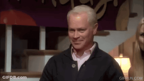 A Man In A Black Sweater Is Smiling In Front Of A Sign That Says " Gifrun.com " GIF
