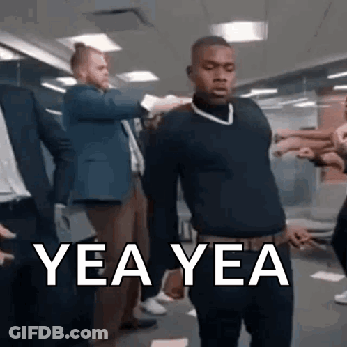 A Man In A Black Sweater Is Standing In A Room With A Group Of People And Says Yea Yea . GIF