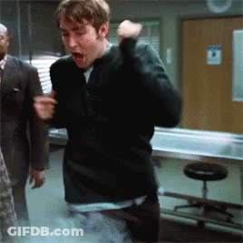 A Man In A Black Sweater Is Standing In A Room With A Sign On The Wall That Says No Smoking GIF