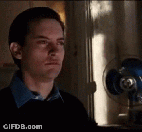 A Man In A Black Sweater Is Standing In Front Of A Fan . GIF
