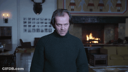 A Man In A Black Sweater Is Standing In Front Of A Fireplace GIF