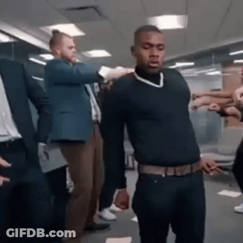 A Man In A Black Sweater Is Standing In Front Of A Group Of People In A Room . GIF
