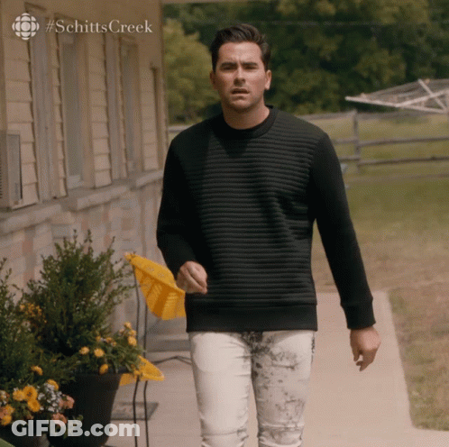 A Man In A Black Sweater Is Walking Down A Sidewalk In Front Of A House With #Schittscreek On The Bottom GIF