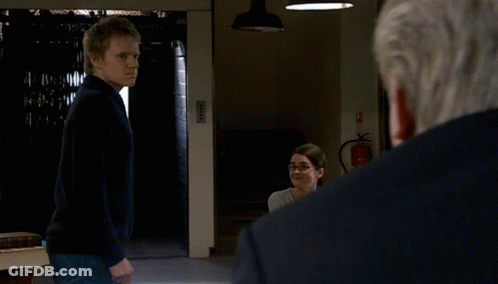 A Man In A Black Sweater Stands In Front Of A Fire Extinguisher In A Dark Room GIF