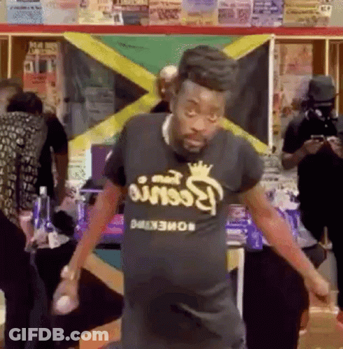 A Man In A Black T-Shirt Is Dancing In Front Of A Flag . GIF
